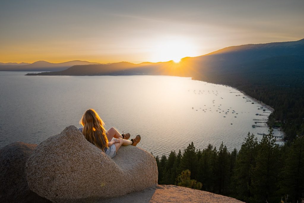 Girl sitting on a rock that looks like a lounge chair at sunset overlooking lake tahoe