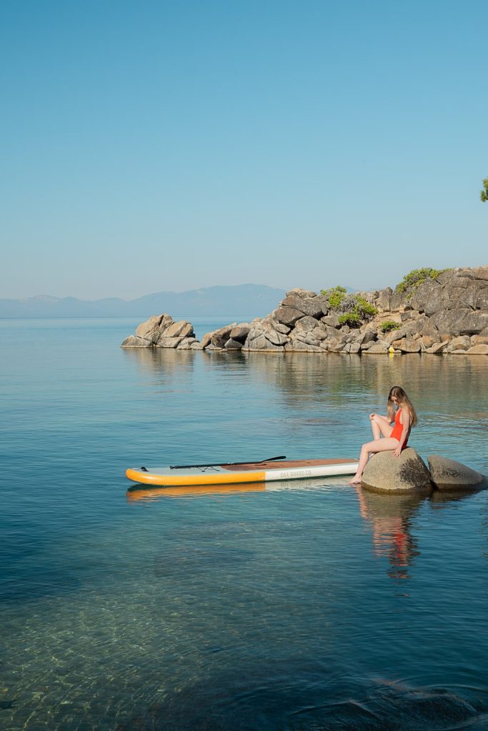 Girl sitting on rock with paddle board in Lake Tahoe