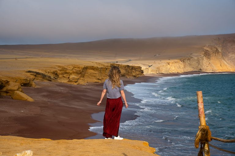 girl standing on a cliff overlooking the red beach in Paracas Peru