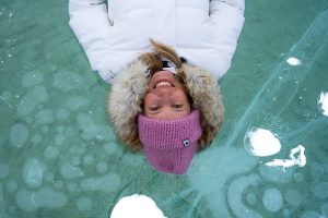 girl in pink beanie lying down on top of the ice at Abraham Lake with frozen bubbles above her head